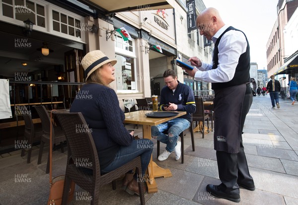 260421 Bars and restaurants reopen, Wales - Manager Mark Falzon serves Sally Bingham and Paul Lovelock from Beddau, the first customers at Cardiff's The Old Arcade pub, as bars and restaurants in Wales are allowed to serve customers outdoors after a lifting of Welsh Government COVID-19 restrictions today