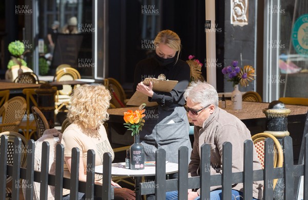 260421 Bars and restaurants reopen, Wales - Staff at bars and restaurants in Cardiff serve customers after a lifting of Welsh Government COVID-19 restrictions today allowing the establishments to serve food and drink outdoors
