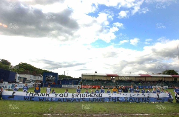 240503 - Bridgend v Pontypridd - Welsh Premiership - The Junior Ravens show a banner of support at the Brewery Field on Bridgend's final home game as a professional club