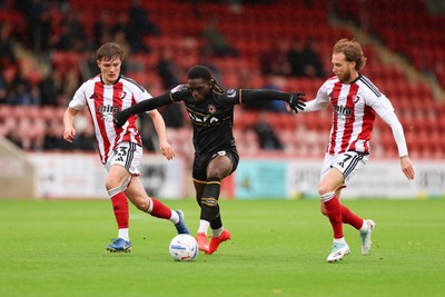 241026 Cheltenham Town v Newport County, EFL Sky Bet League 2 -  Michael Adu-Poku of Newport County gets between Freddy Willcox of Cheltenham Town and Ben Stevenson of Cheltenham Town