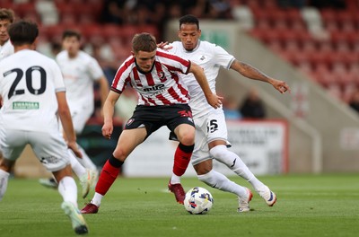 230725 - Cheltenham Town v Swansea City - Pre Season Friendly - Freddy Willcox of Cheltenham Town is tackled by Ronald of Swansea City 