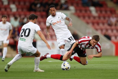 230725 - Cheltenham Town v Swansea City - Pre Season Friendly - Freddy Willcox of Cheltenham Town is tackled by Ronald of Swansea City 
