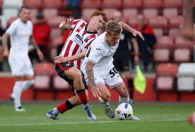 230725 - Cheltenham Town v Swansea City - Pre Season Friendly - Ethan Galbraith of Swansea City is tackled by Harry Tustin of Cheltenham Town 