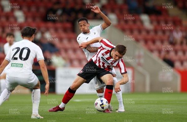 230725 - Cheltenham Town v Swansea City - Pre Season Friendly - Freddy Willcox of Cheltenham Town is tackled by Ronald of Swansea City 