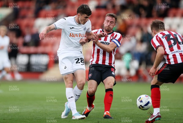 230725 - Cheltenham Town v Swansea City - Pre Season Friendly - Joel Cotterill of Swansea City is tackled by Luke Young of Cheltenham Town 