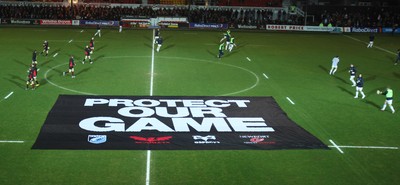 261213 - Newport Gwent Dragons v Cardiff Blues, RaboDirect PRO12 - Dragons and Blues players warm up as protest banner is placed on the pitch before the start of the match