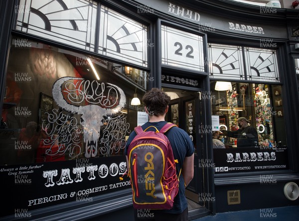 150321 - Customers queue at Swyd Tattoo and Barber Shop in Cardiff city centre as barbers and hairdressers on the first day they are allowed to reopen in Wales after the Welsh Government relaxed COVID19 lockdown restrictions in the country Restrictions relating to tattoos have yet to be lifted
