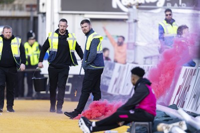 220225 - Newport County v Cheltenham Town - Sky Bet League 2 - A steward responds to a flare thrown by Cheltenham Town supporters celebrating their first goal