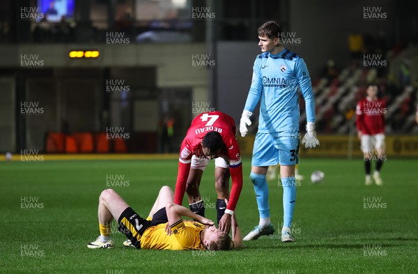 120324 - Newport County v Morecambe, EFL Sky Bet League 2 - Will Evans of Newport County is checked by Jacob Bedeau of Morecambe and Archie Mair of Morecambe after picking up an injury