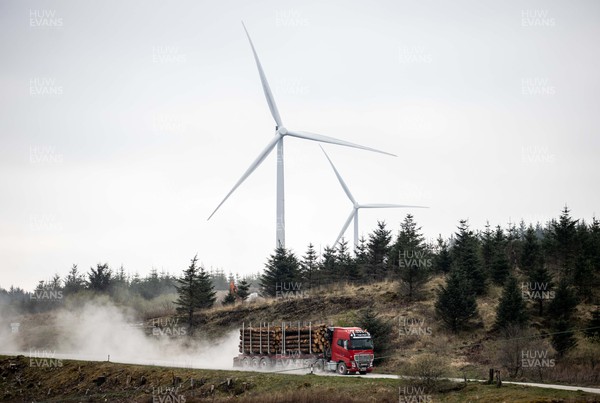 220422 - Picture shows a HGV logging lorry driving in front of wind turbines on forestry land in South Wales, UK The renewable energy is key for providing green energy to homes as the Welsh Government pushes to net zero carbon emissions by 2050
