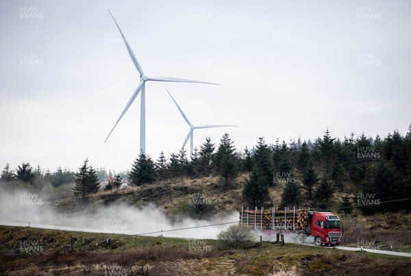 220422 - Picture shows a HGV logging lorry driving in front of wind turbines on forestry land in South Wales, UK The renewable energy is key for providing green energy to homes as the Welsh Government pushes to net zero carbon emissions by 2050