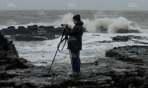 100321 A photographer takes photographs as rough seas pound the coastline around the lighthouse at Porthcawl, south Wales as large parts of the country are expected to hit by rain and strong winds overnight