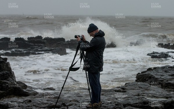 100321 A photographer takes photographs as rough seas pound the coastline around the lighthouse at Porthcawl, south Wales as large parts of the country are expected to hit by rain and strong winds overnight