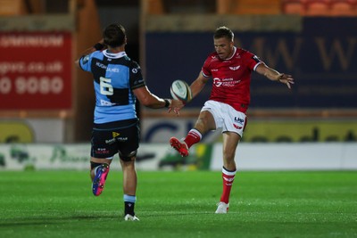 260926 - Scarlets v Cardiff Rugby - United Rugby Championship - Gareth Anscombe of Scarlets kicks the ball as Alex Mann of Cardiff closes in