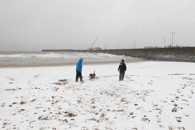 180113 - Snow in South Wales - Gail and Wayne Morris walk their dog in the snow on the beach at Porthcawl