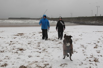 180113 - Snow in South Wales - Gail and Wayne Morris walk their dog in the snow on the beach at Porthcawl