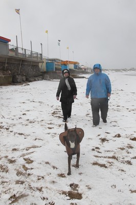 180113 - Snow in South Wales - Gail and Wayne Morris walk their dog in the snow on the beach at Porthcawl