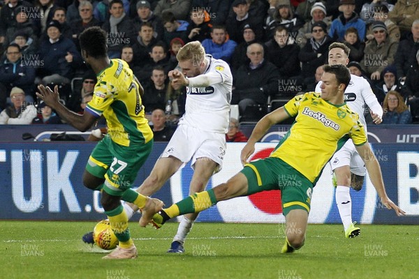 241118 - Swansea City v Norwich City, EFL Championship - Oliver McBurnie of Swansea City (centre) shoots at goal despite the attentions of Christoph Zimmermann of Norwich City (right)