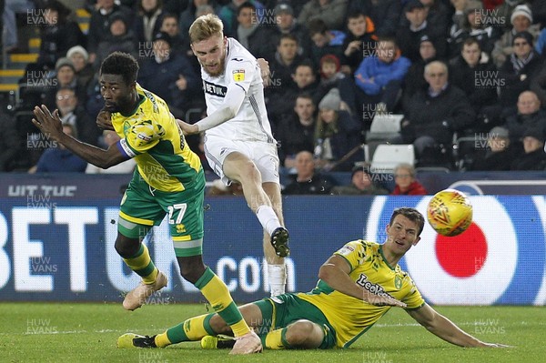 241118 - Swansea City v Norwich City, EFL Championship - Oliver McBurnie of Swansea City (centre) finds room to shoot at goal between Alexander Tettey (left) and Christoph Zimmermann of Norwich City