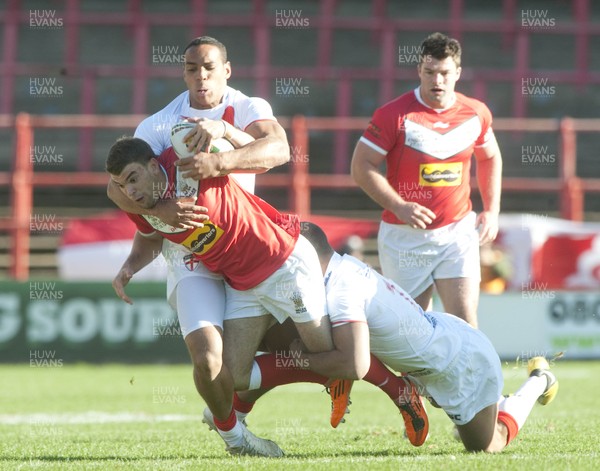 251012 -  Wales v England - Rugby League -     Elliot Kear of Wales, centre, is tackled by Leroy Cudjoe, left and Gareth Ellis of England  