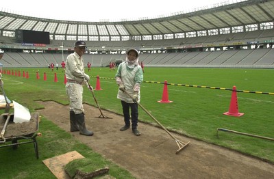 120601 - Wales Rugby Training - A female worker lays turf at the Tokyo Stadium while the team trains in readiness for the game against the Pacific Barbarians on Wednesday