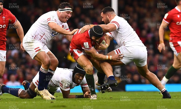 250223 - Wales v England - Guinness Six Nations 2023 - Leigh Halfpenny of Wales is tackled by Jamie George and Ellis Genge of England