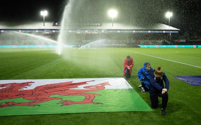 281025 - Wales v Poland, Women’s International Challenge Match - Members of the flag team at a soaking at the start of the match as the pitch sprinklers turn in their direction