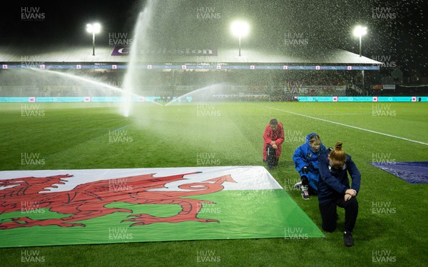281025 - Wales v Poland, Women’s International Challenge Match - Members of the flag team at a soaking at the start of the match as the pitch sprinklers turn in their direction