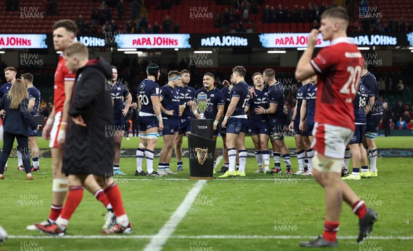030224 - Wales v Scotland, Guinness Six Nations 2024 - The Scotland team wait to lift the Doddie Weir Cup as Wales players walk past