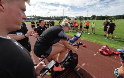 240823 - Wales Women Training session - Team mates look on as Carys Williams-Morris finishes a set on the bike during training session