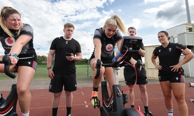 240823 - Wales Women Training session - Team mates look on as Carys Williams-Morris finishes a set on the bike during training session